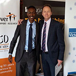 2 men in suits standing in front of pull up banner