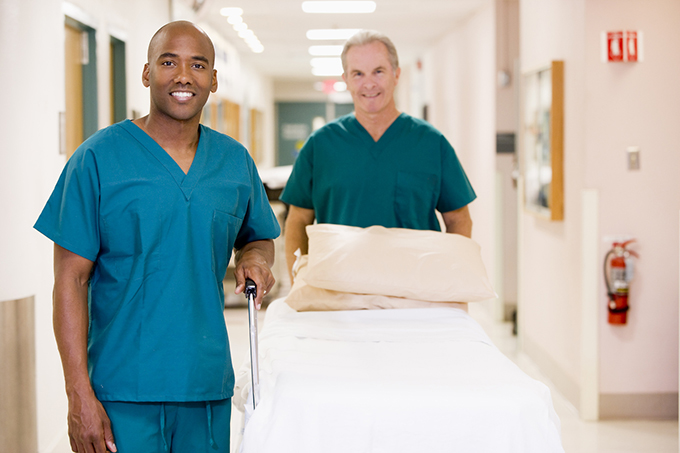 Two Orderlies Pushing An Empty Bed Down A Hospital Corridor Smiling