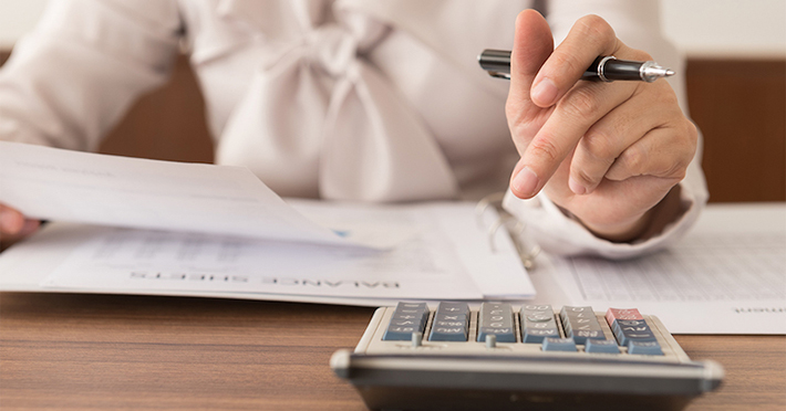 Hand holding a pen and a calculator on the table 