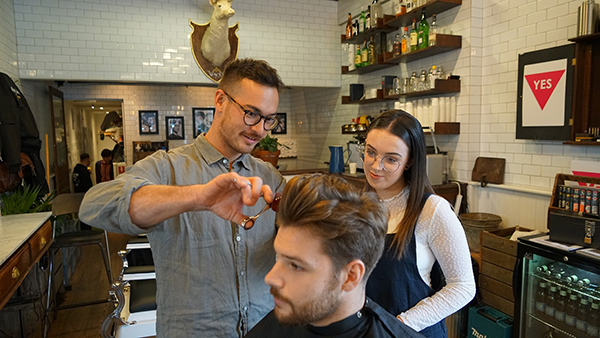Male barber and female apprentice cutting man's hair 