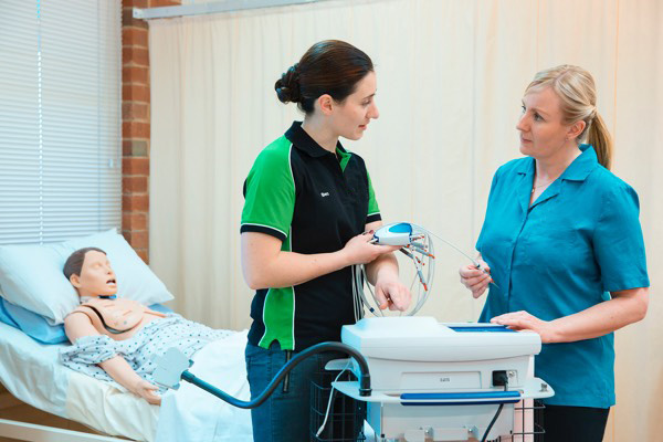 Teacher and student discussing with a fake patient in the background