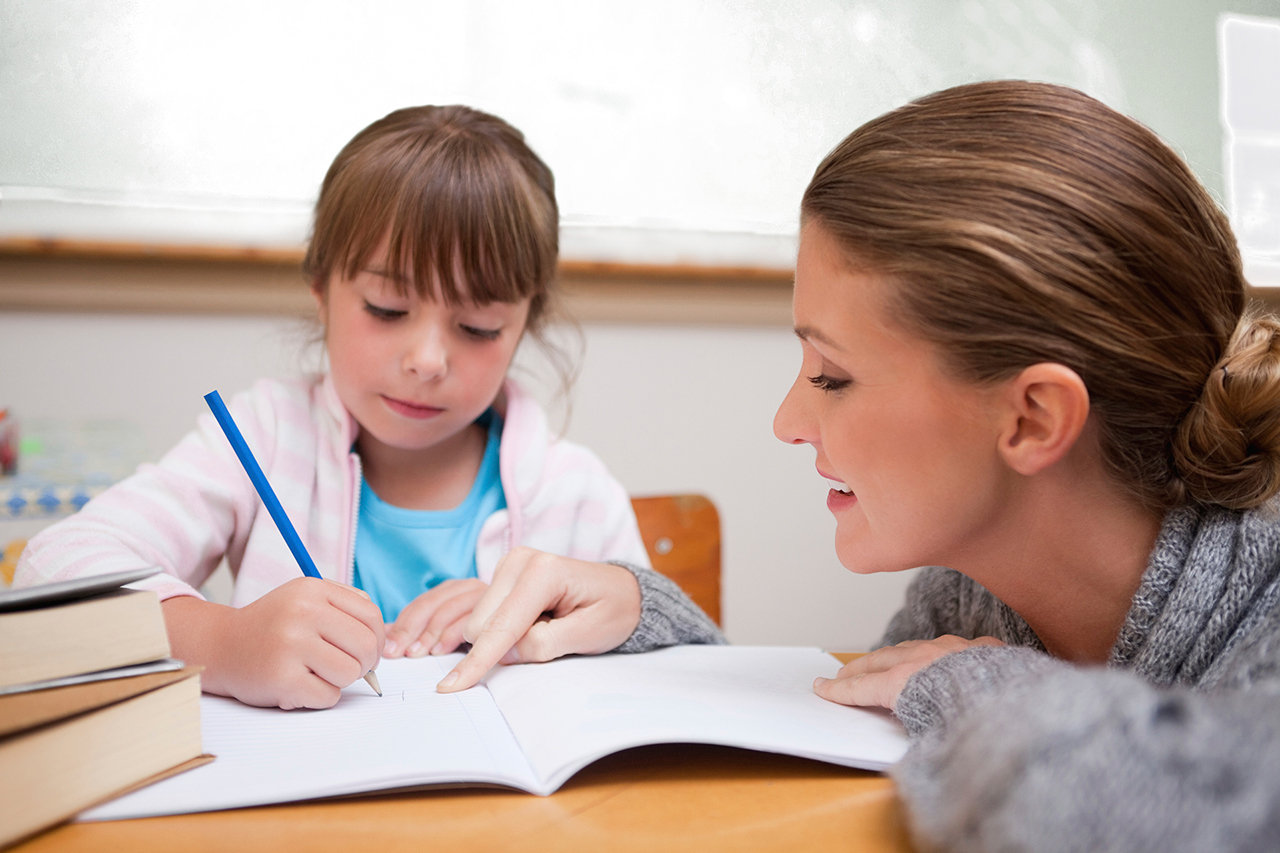 Cute schoolgirl writing a while her teacher is talking in a classroom