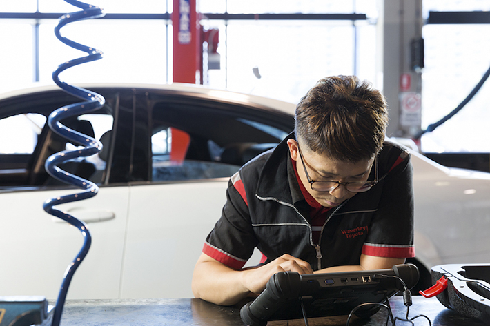 Auto mechanic doing some testing on a device next to a car