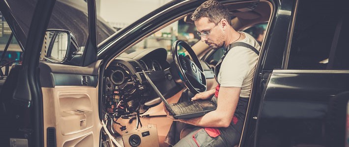 Auto electrician sitting in side car seat and doing test on laptop