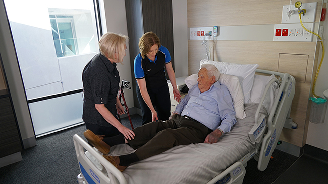 2 female health care workers helping elderly man