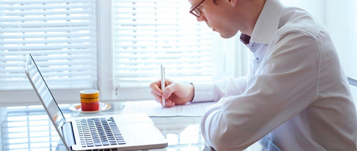 Young man next to a laptop and writing on paper 