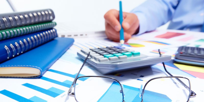 Close up of files and calculator, with person in the background working on a graph