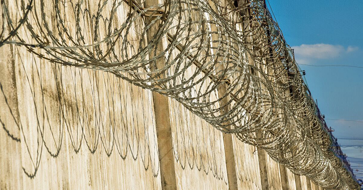 Image of a prison wall with barb wire at the top 