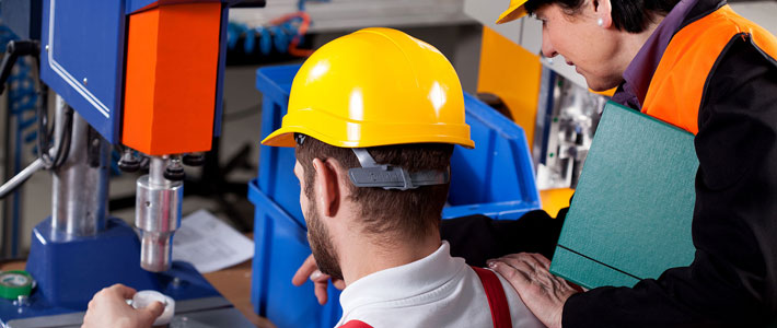 Two workers in hard hats, one using a drill and one watching