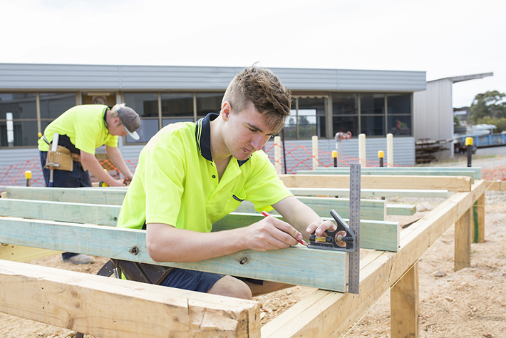 Young male apprentice measuring up a piece of wood 